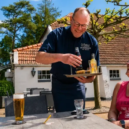 Medewerker van het campingrestaurant serveert een borrelplank op het zonnige terras