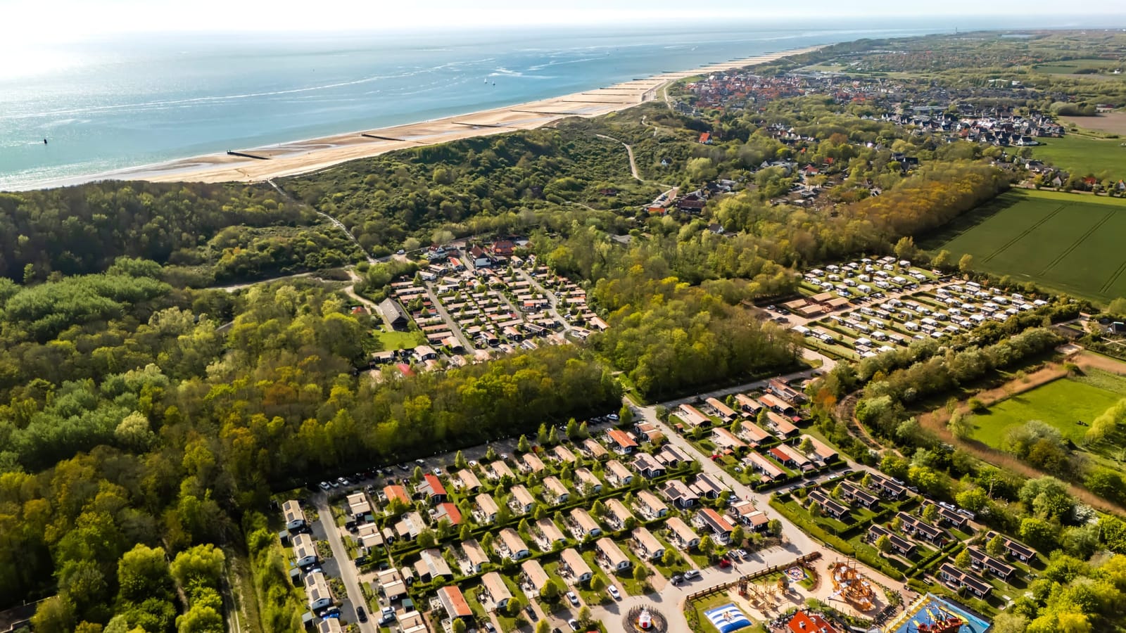 Luchtfoto van Vakantiepark De Meerpaal in Zoutelande, met chalets en het speelschip, de duinen en het strand op de achtergrond