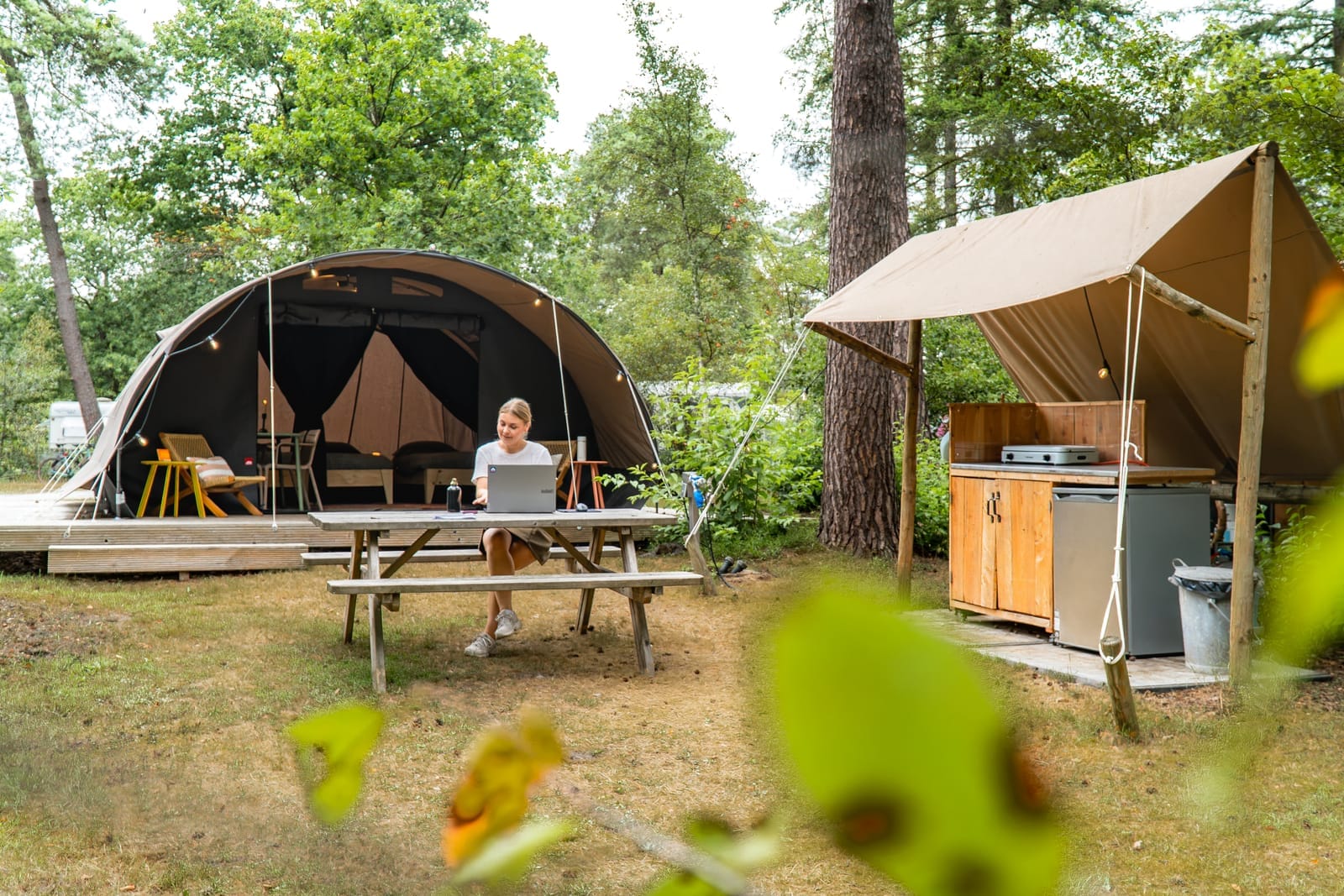 Gasten aan tafel bij hun caravan op een camping tussen de bomen