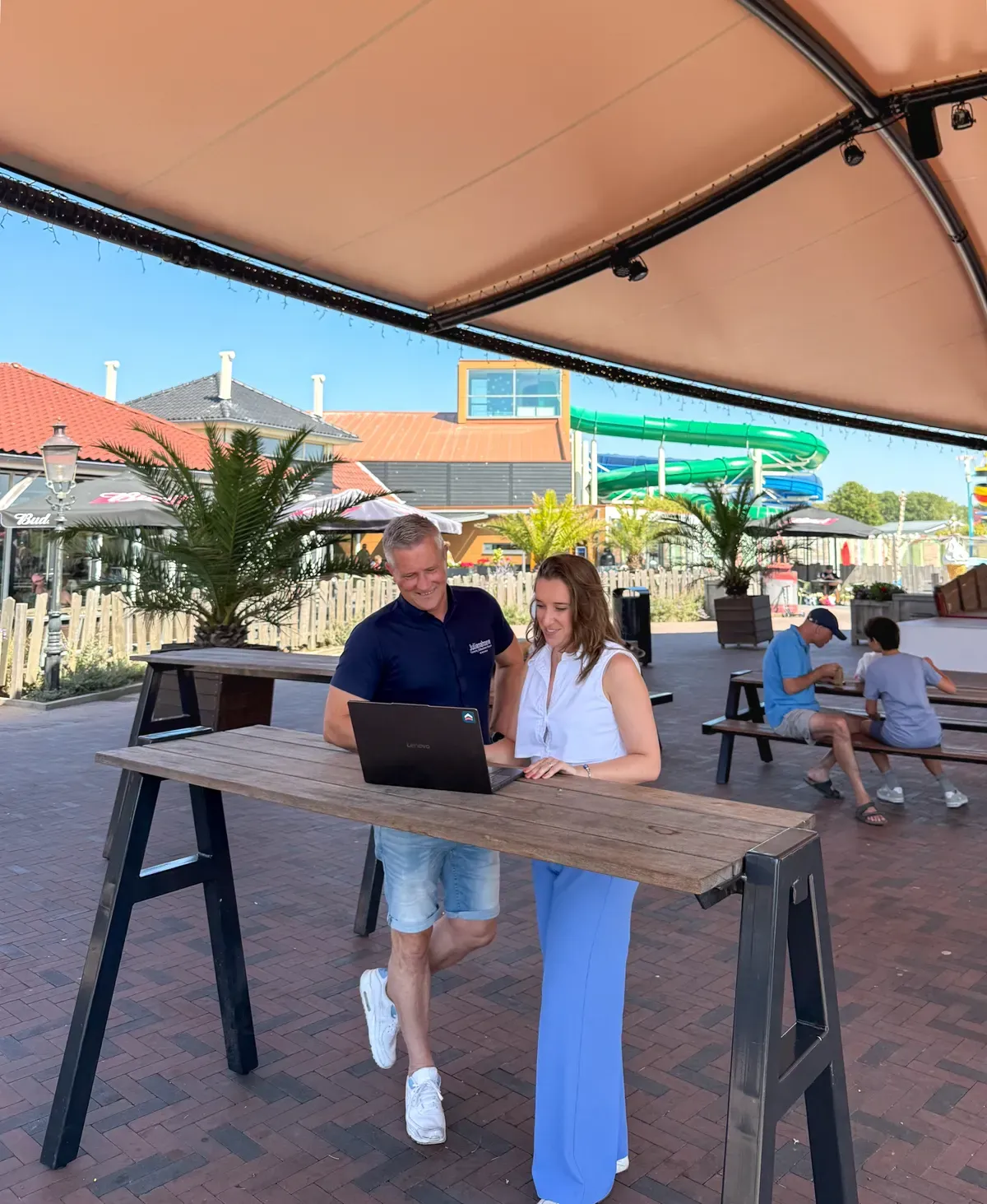 Marketeer van UPPER kijkt samen met de campingeigenaar op een laptop naar de campagnes, op het terras van het park