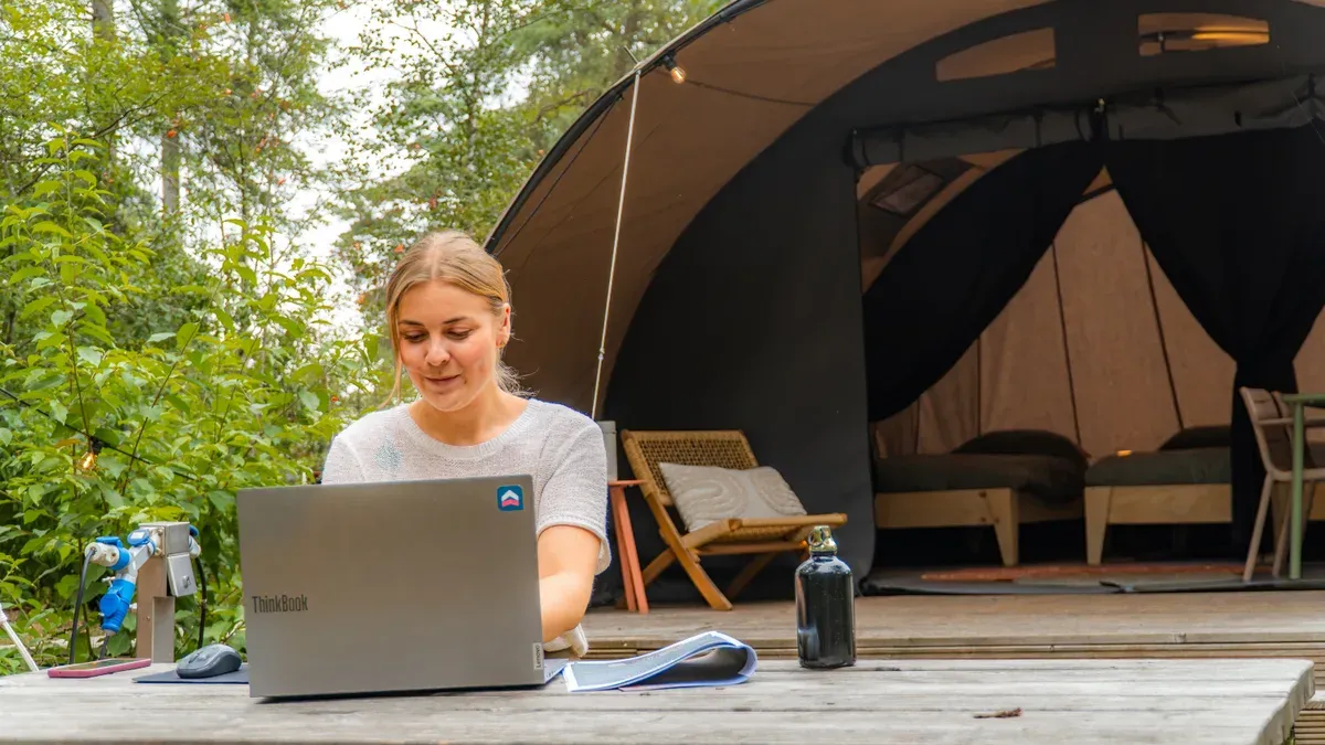 Marketeer van UPPER werkt op een laptop bij een safaritent op de camping